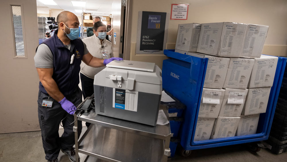 Man in scrubs pushes cart holding a cooler.