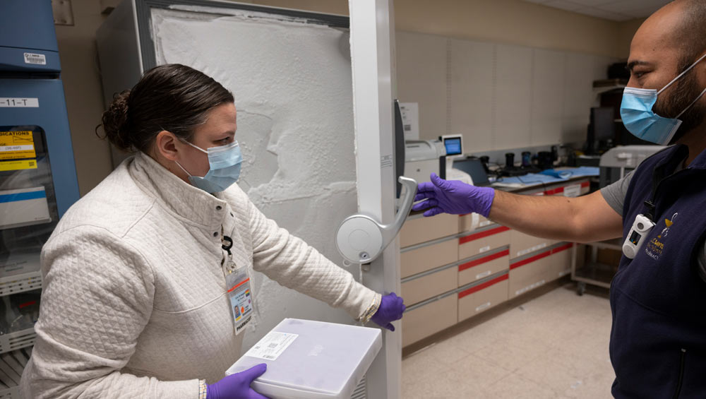 Woman in lab coat removes tray from freezer.