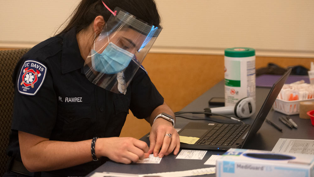 Student EMT (in uniform) fills out vaccination card.