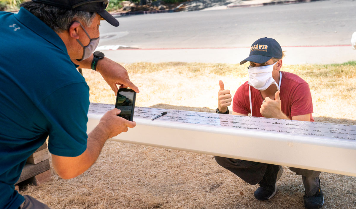 Man takes photo of co-worker giving thumbs-up after signing the beam.