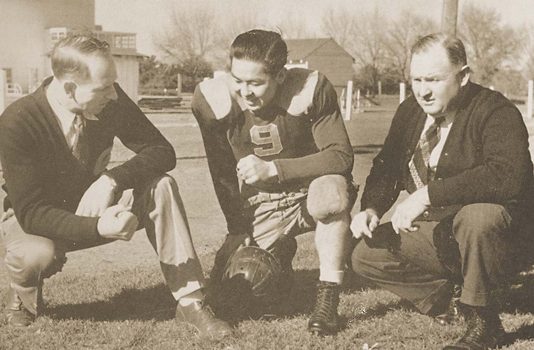 Two coaches speak with a football player, 1939