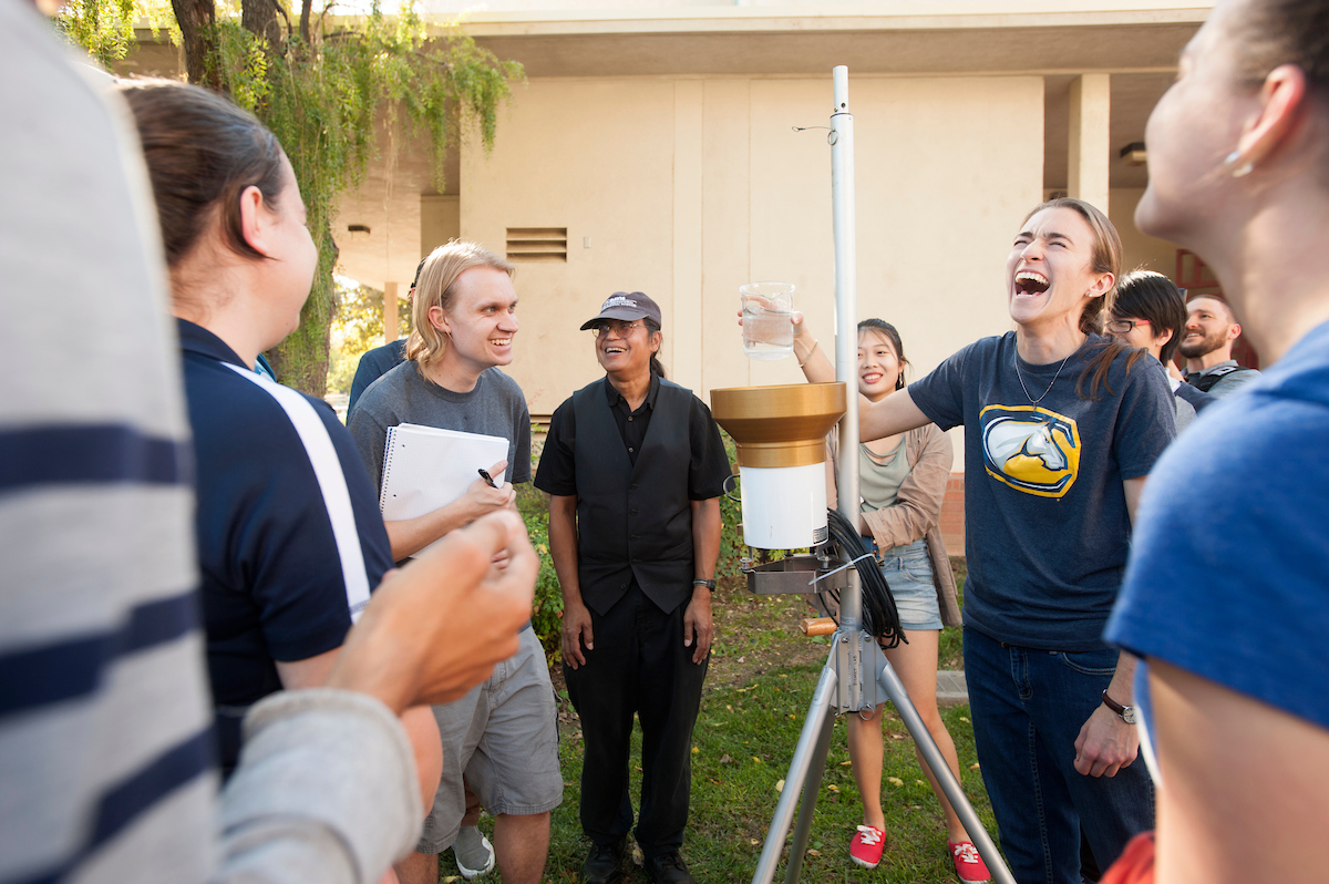 Students and teachers laugh outside while holding a tall instrument at UC Davis. 