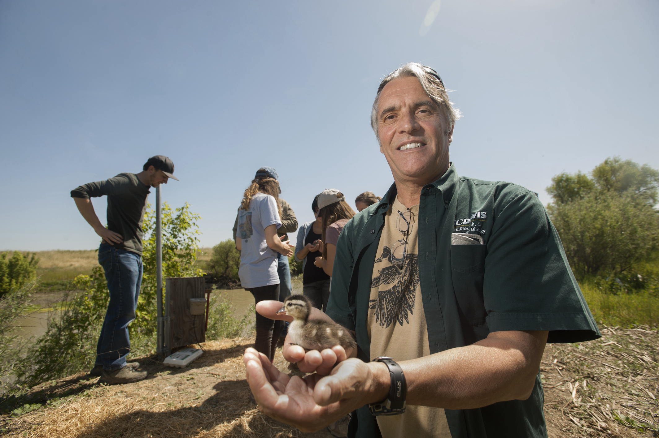 Professor John Eadie holds duckling with students in background outside