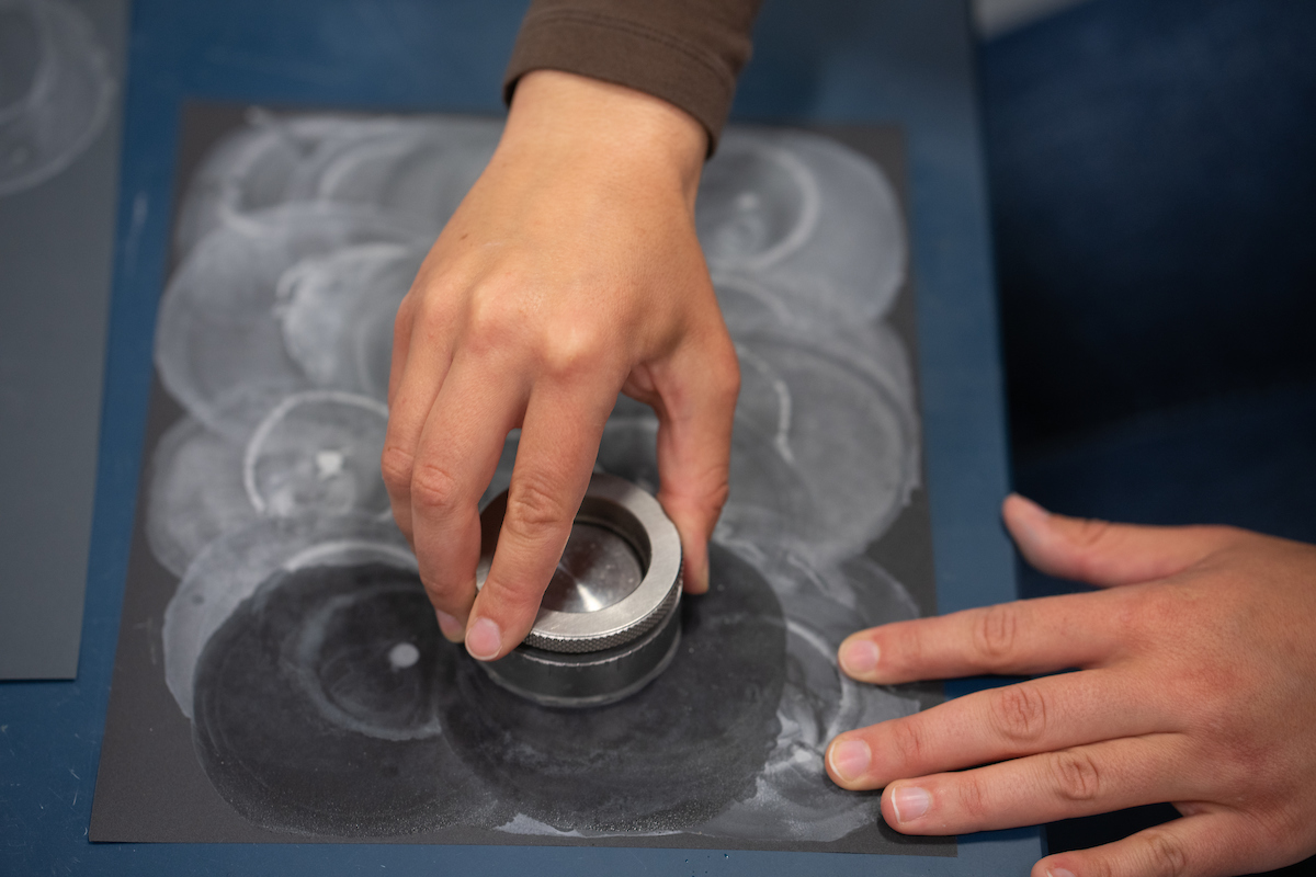 hands grind fish otolith on sandpaper using circular device