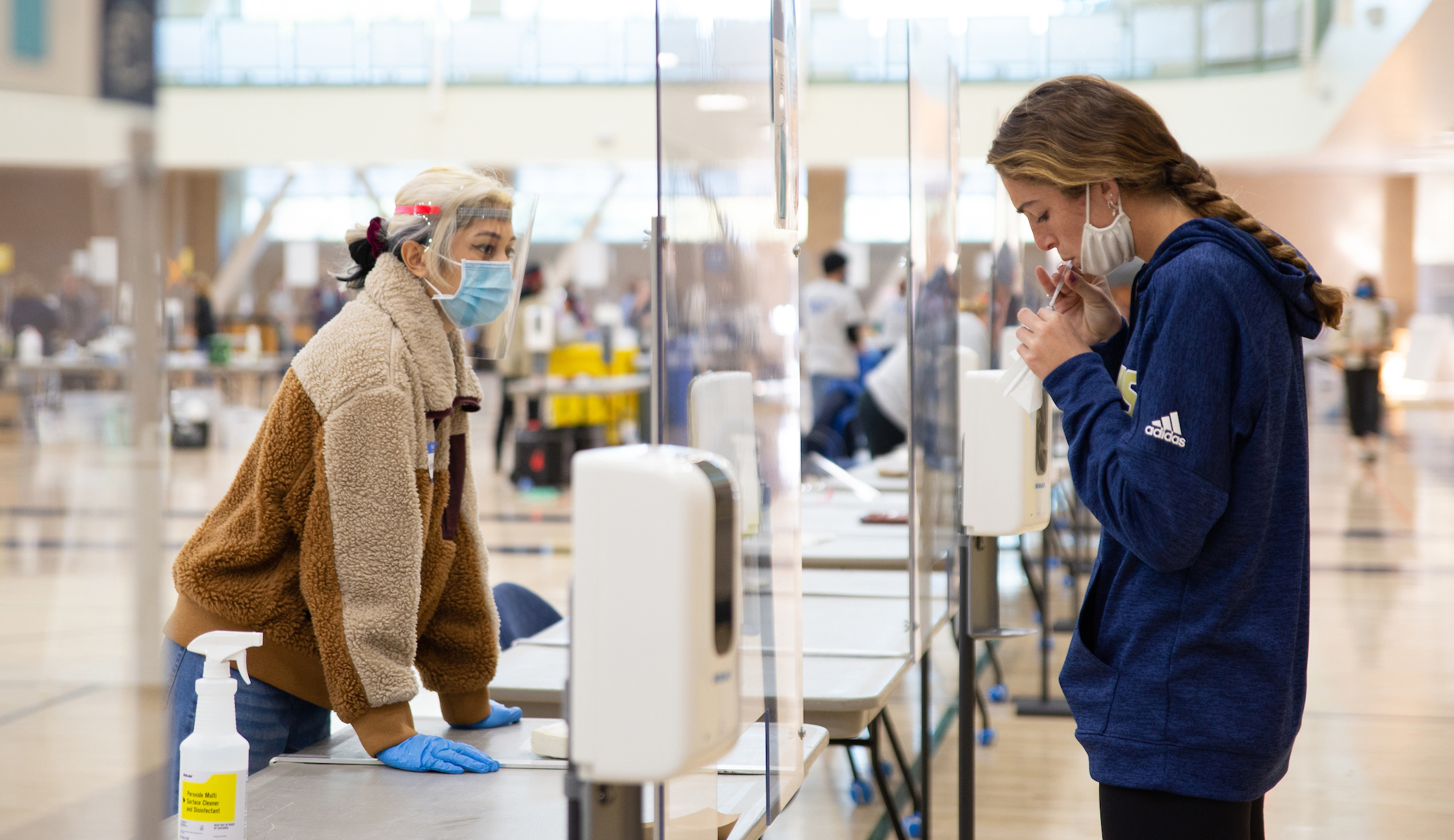 A student spits into a tube while another oversees the test.