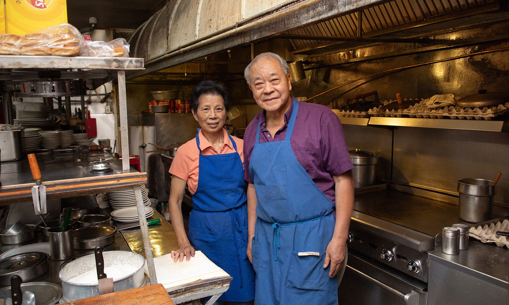 Two people stand in an old kitchen