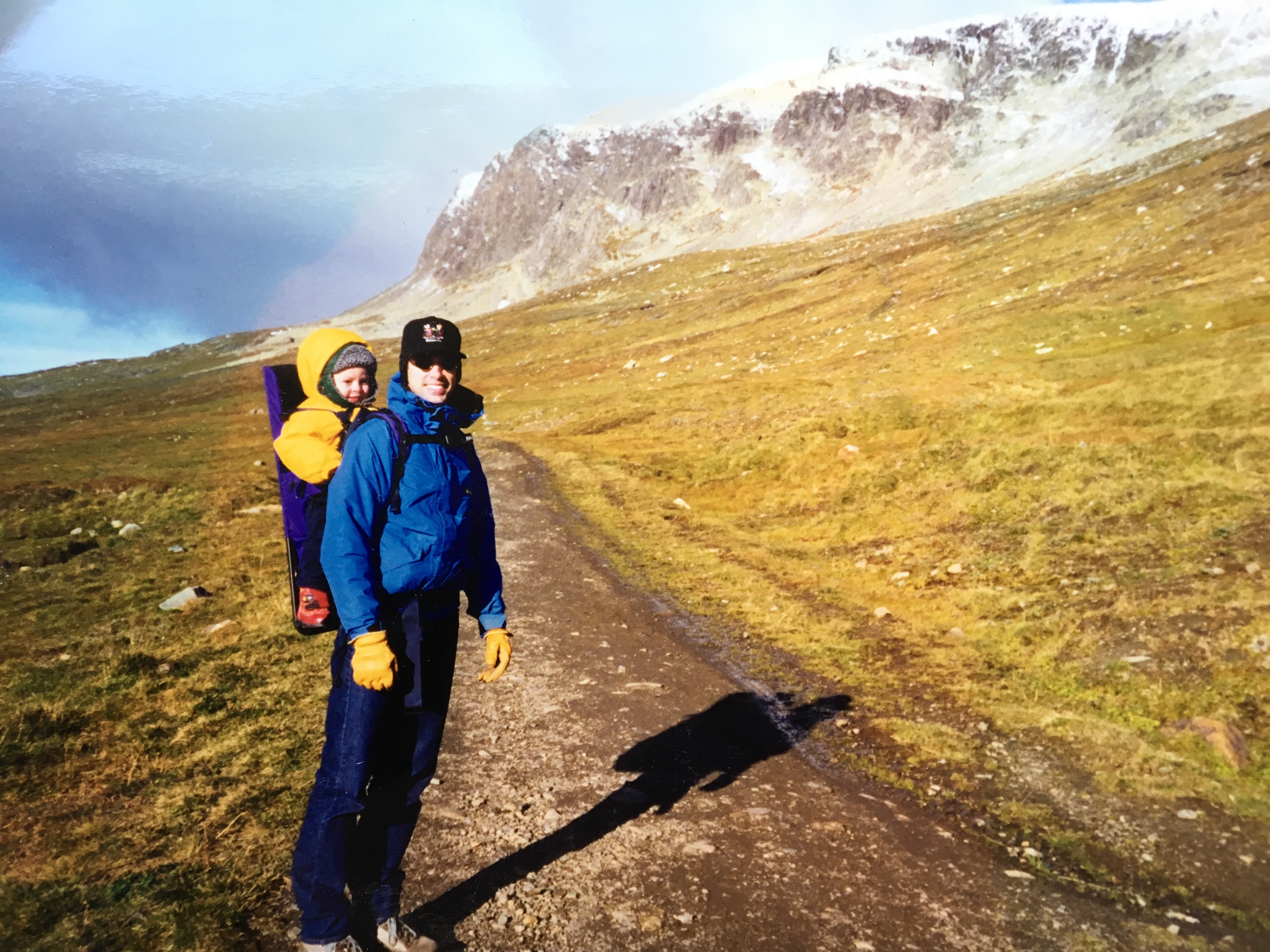 Man with baby in backpack in Norway with snowy mountains in background