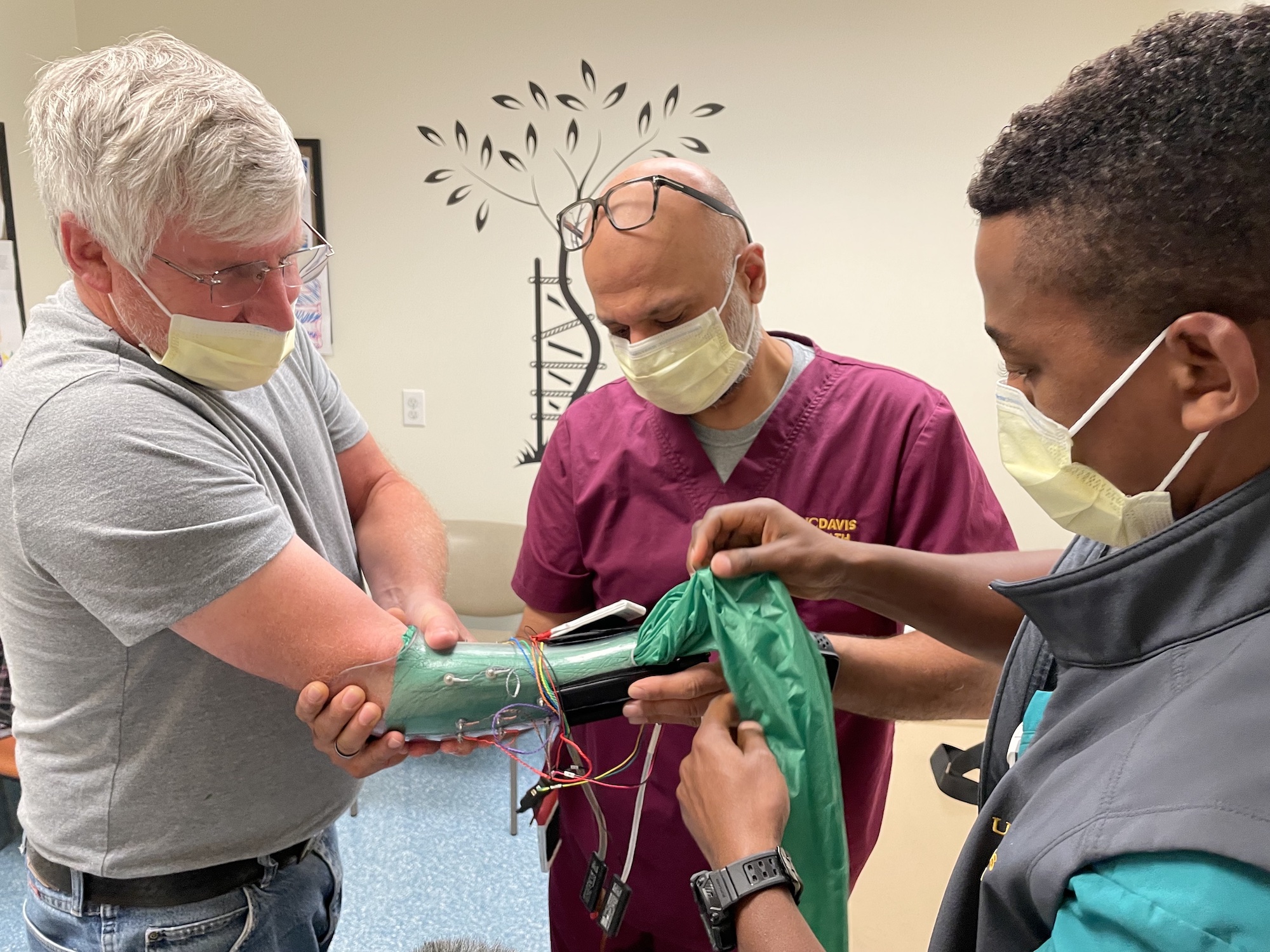 David Brockman puts his arm into a carbon fiber sleeve that will attach to his prosthetic hand. Fehran Maher and Laduan Smedley, both certified prosthetists, help him with the fitting.