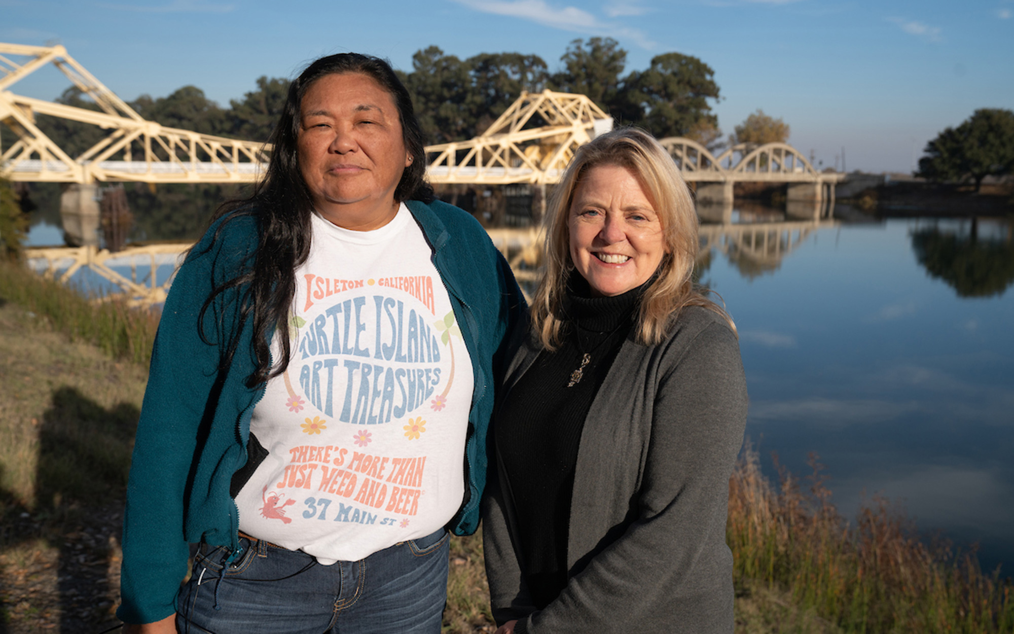 Two women stand by waterway and bridge