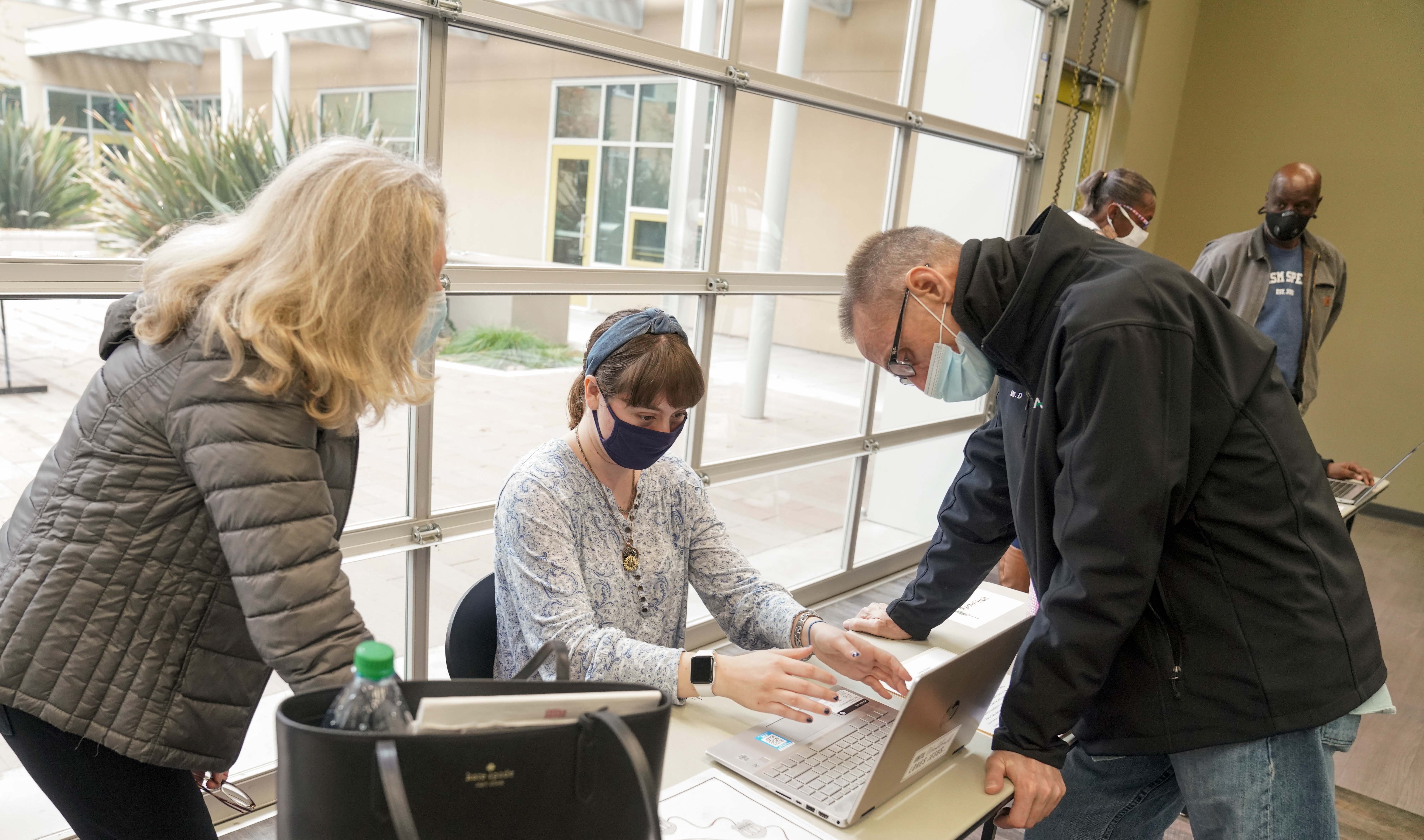 A person sits at a computer while two people look at her work.