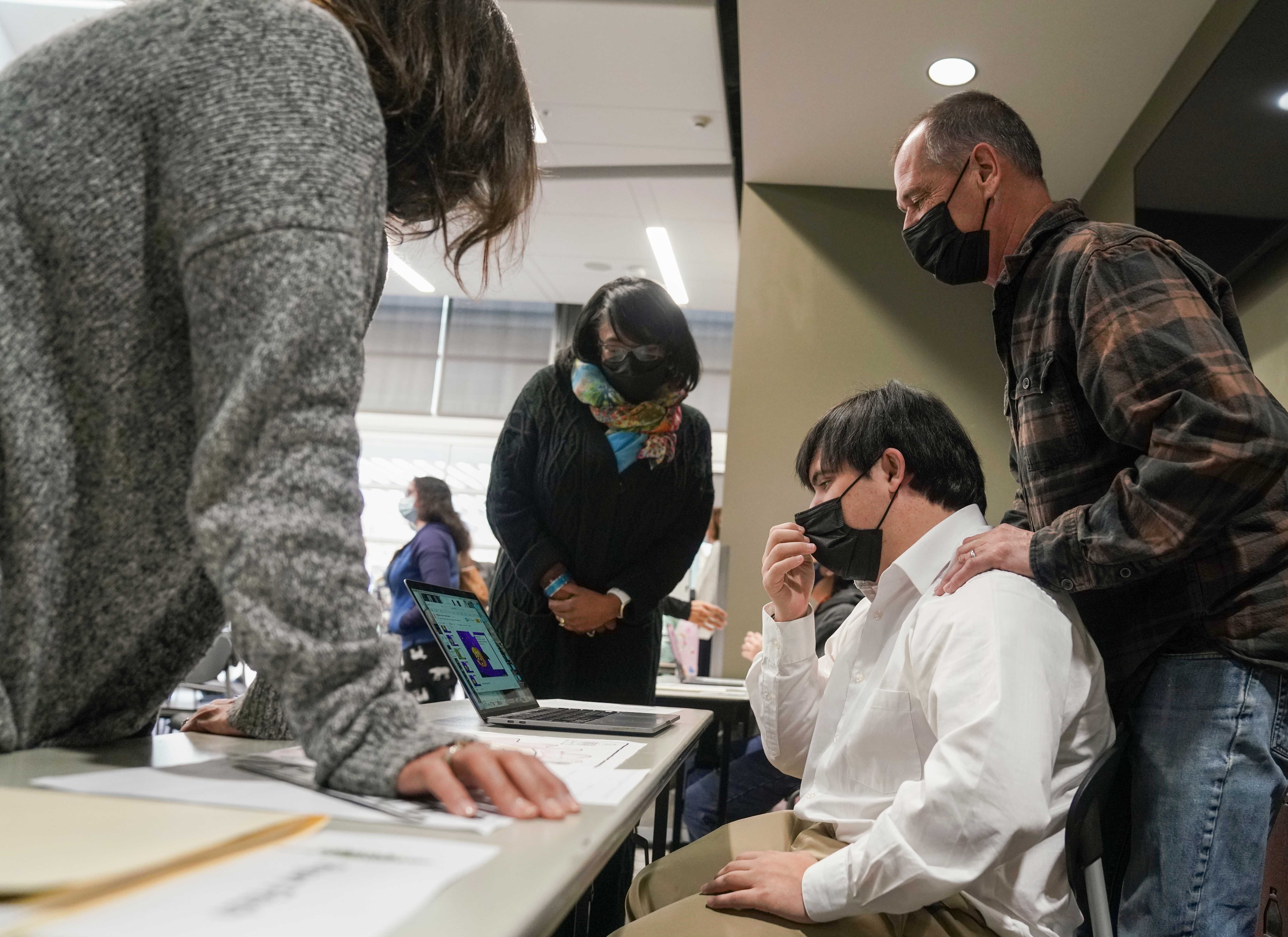 One person sits at a computer while three look at his work