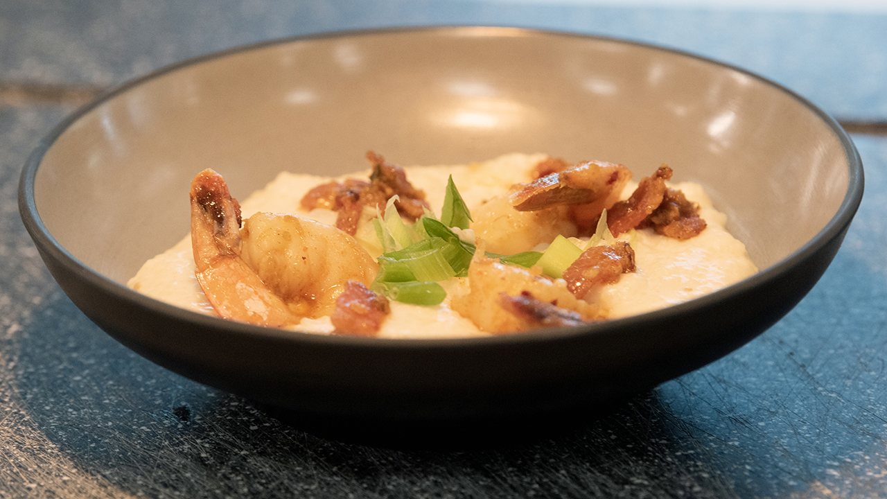 A bowl of Cajun-spiced shrimp over grits with bacon, green onions and chili oil.