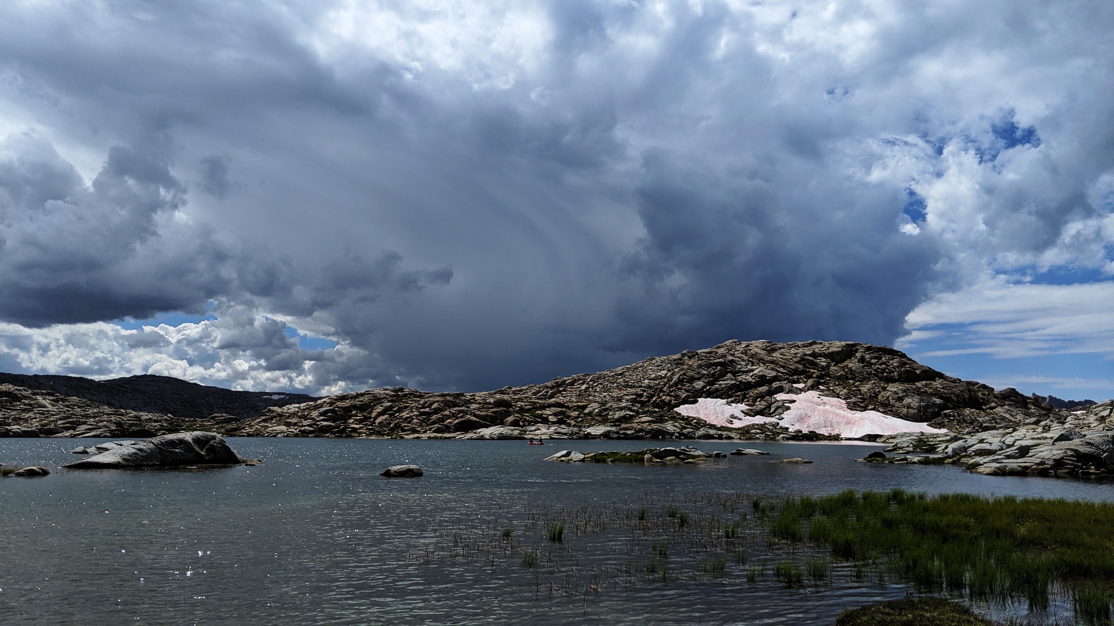 Topaz Lake glistens under a sky of dramaitc, sweeping clouds in the Sierra Nevada mountain range. A small boat is a speck on the water. 