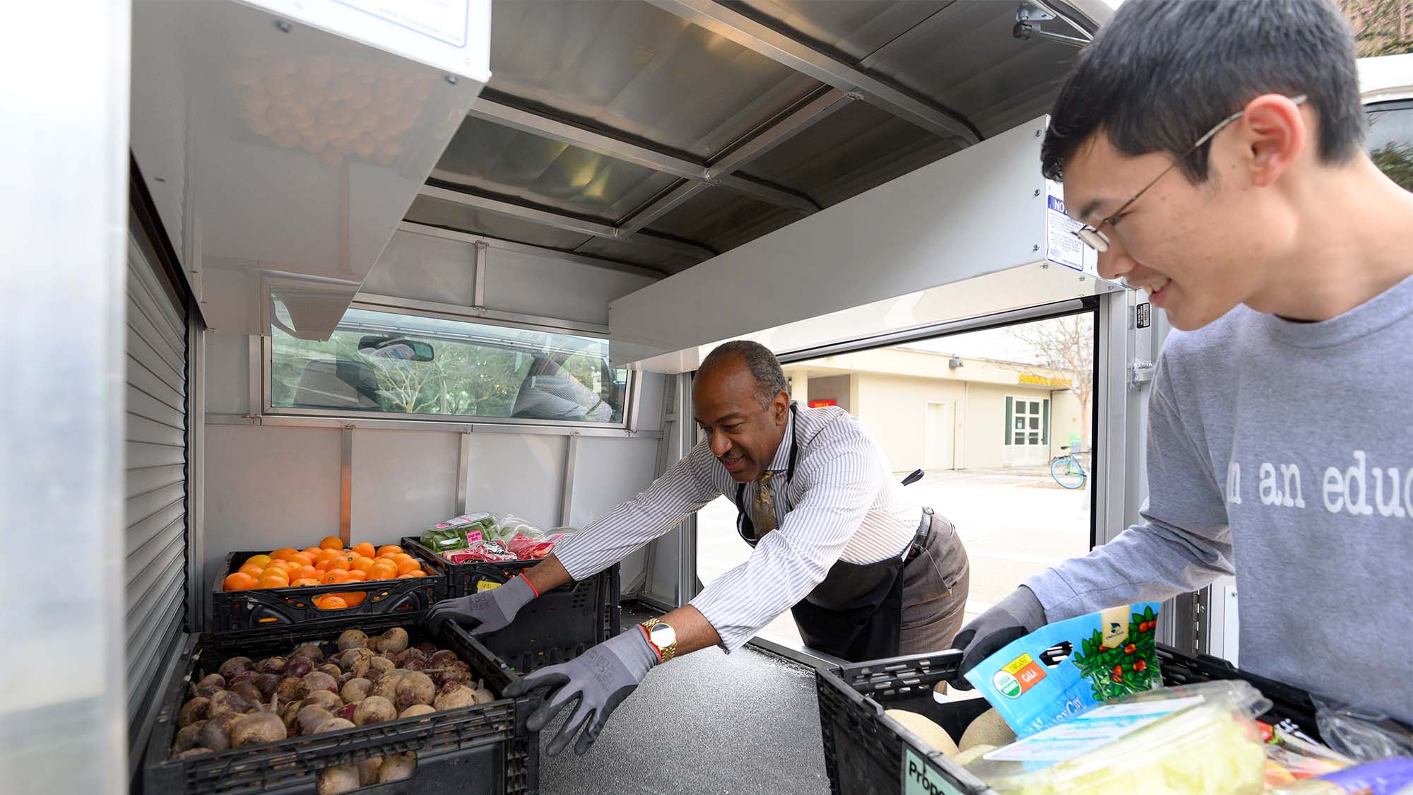 Chancellor Gary S. May unloads a crate of potatoes as a student watches.