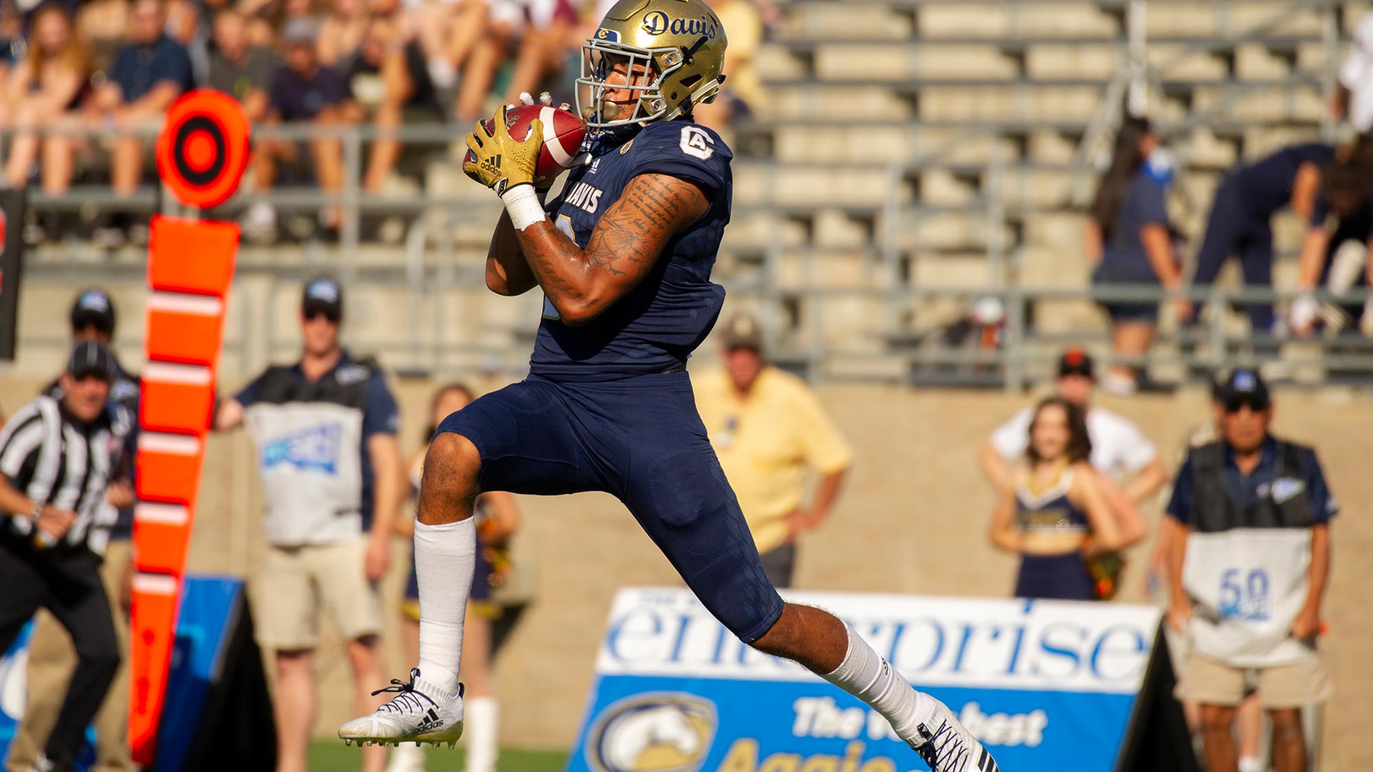 An Aggie football player holds the ball as he leaps over the goal line during a game.