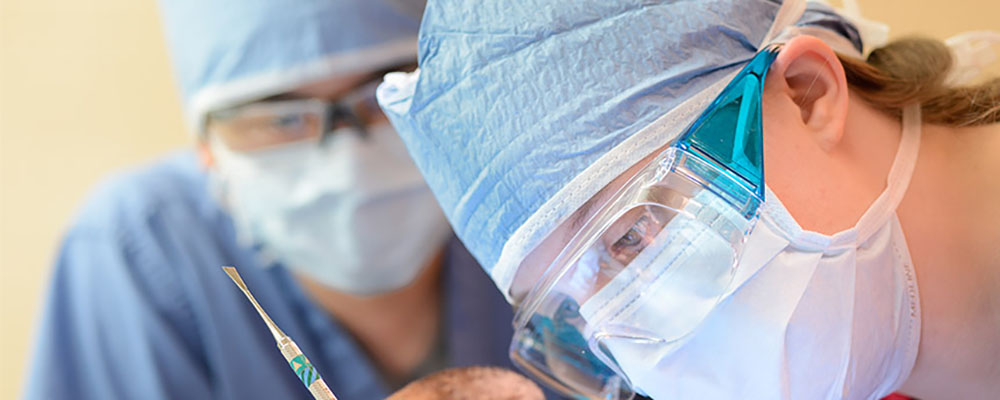 Surgeons in mask concentrate while leaning over. 