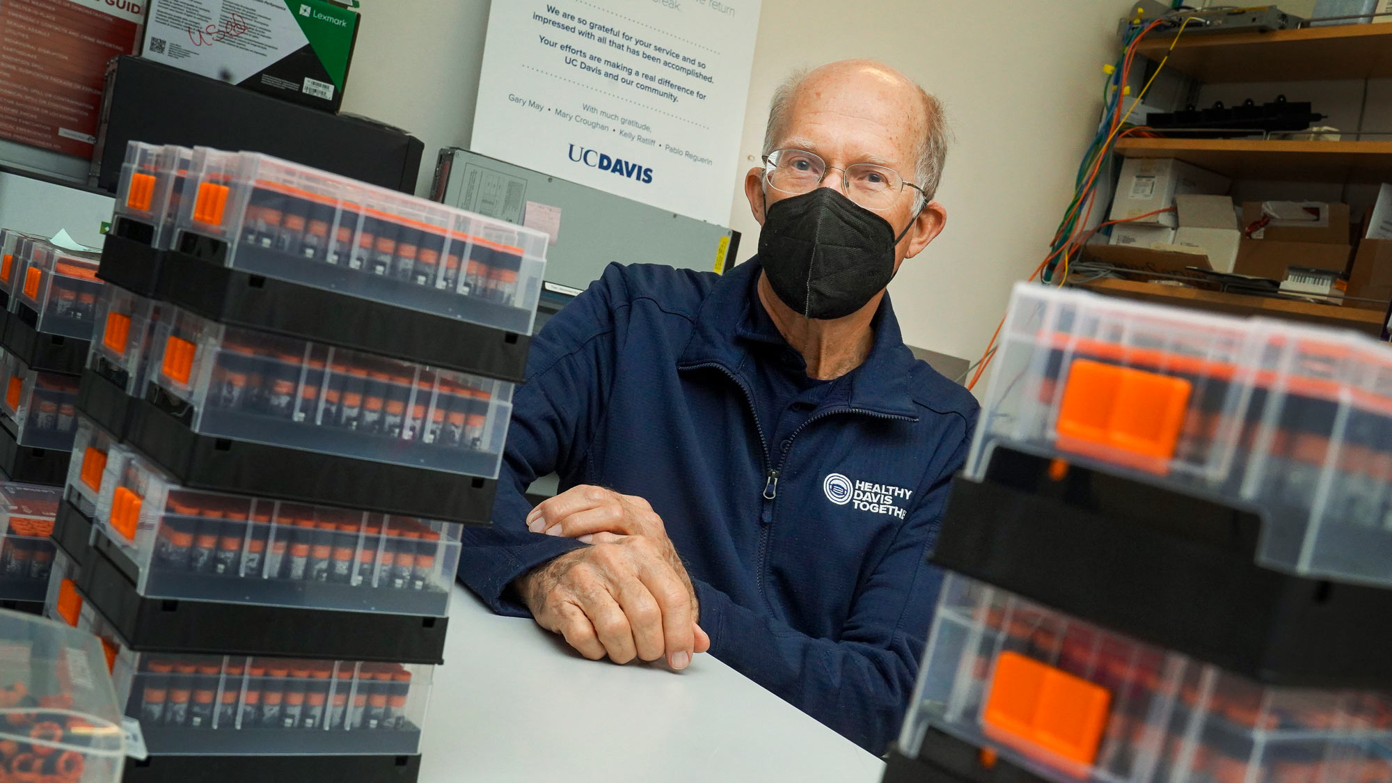 Ken Burtis, in mask, portrait, amid stacks of COVID-19 test specimens in tubes