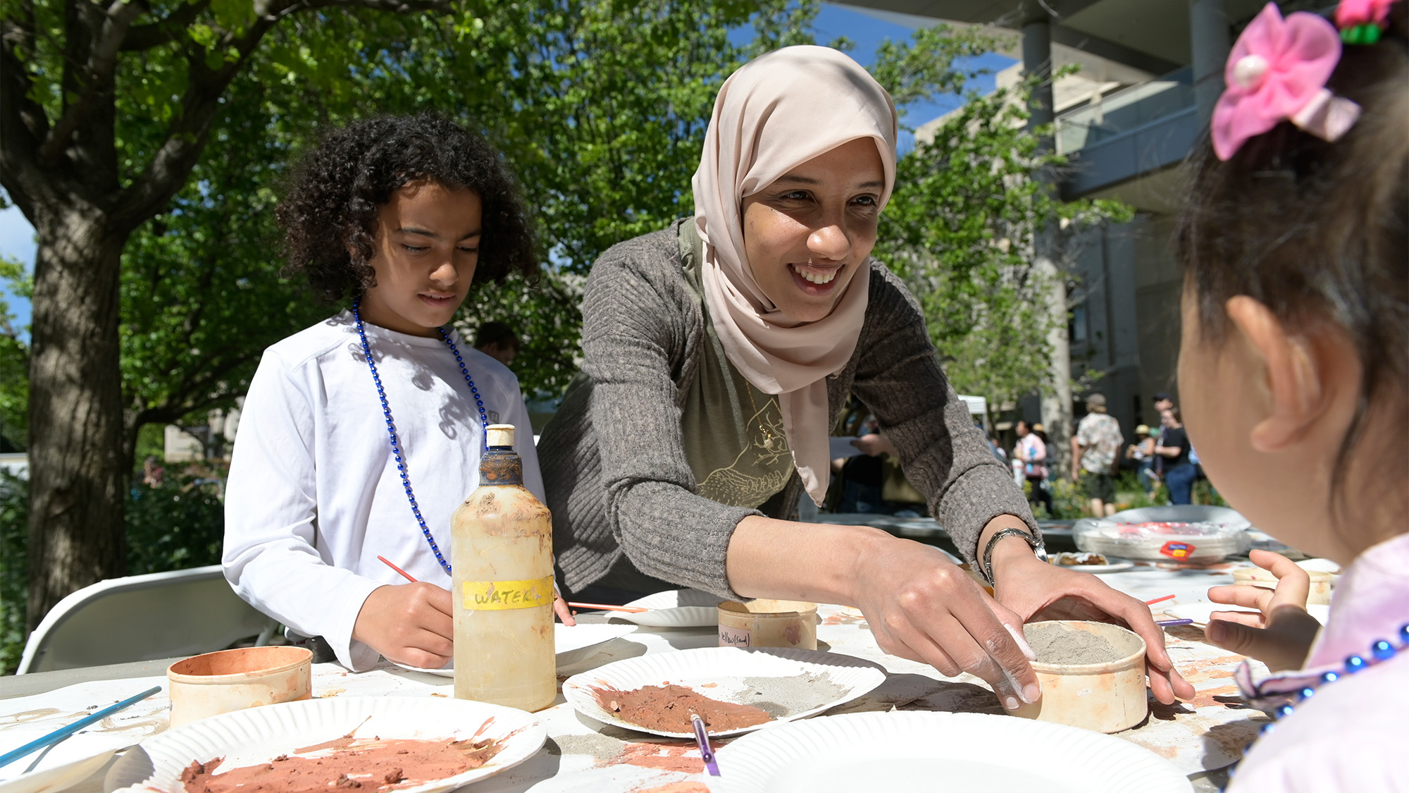 Woman helps children paint with sand.