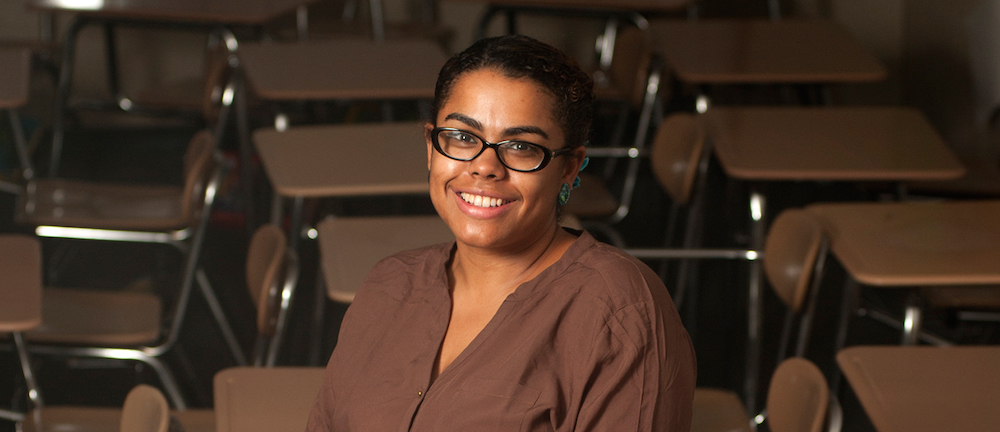 Woman wearing glasses smiles in a classroom. 