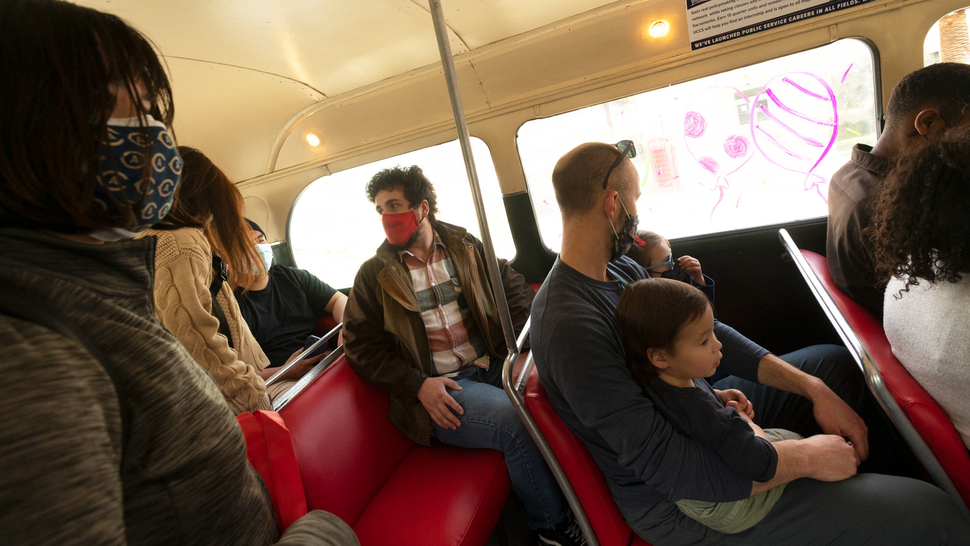 Boy sits on father's lap, aboard vintage double-decker bus