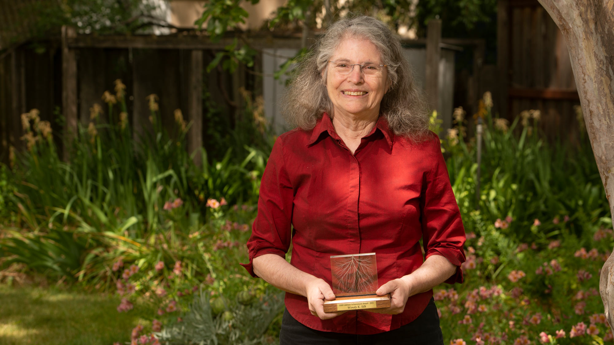 Wendy Kuhn Silk, smiling, holds trophy, in outdoor setting.