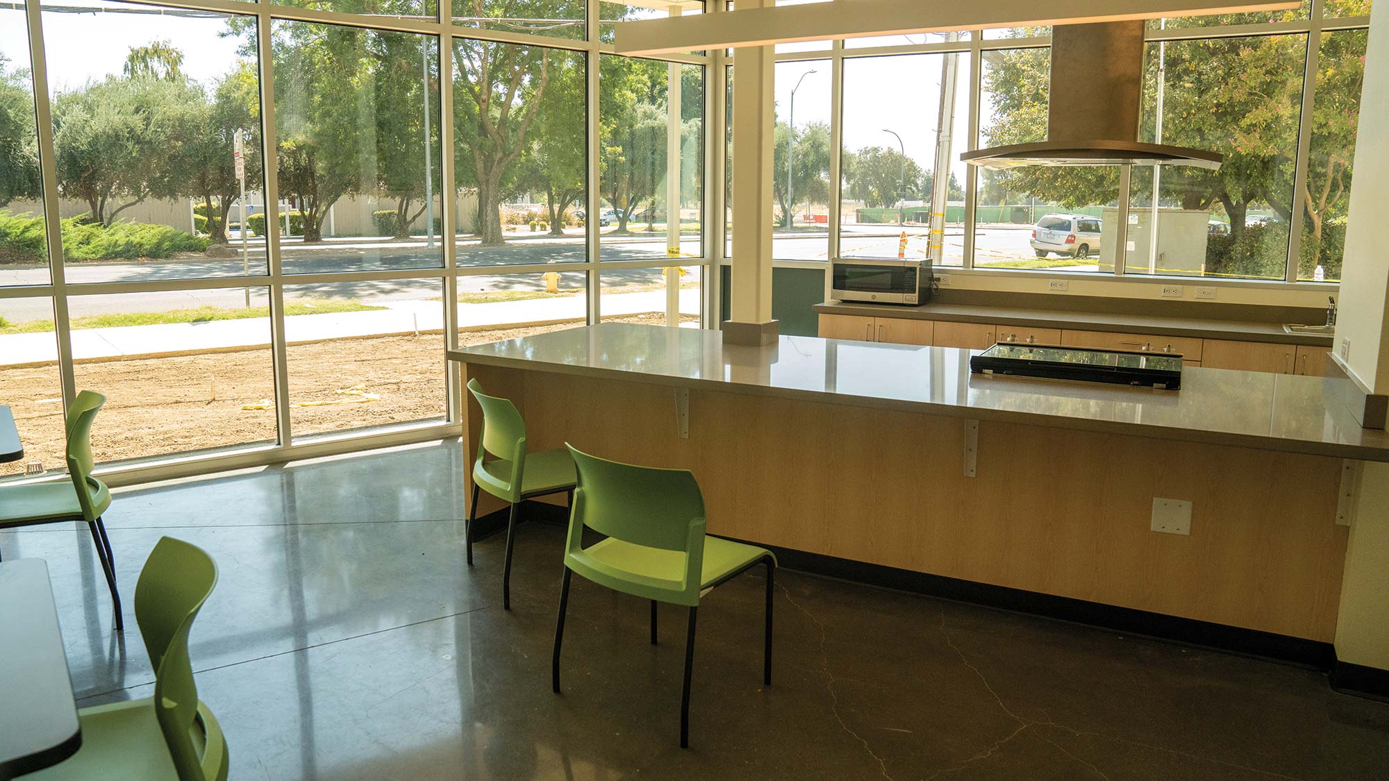 Photo of a new, large communal kitchen. Floor to ceiling windows surround an island with a range and hood.