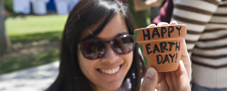 A woman sitting outside shows her Earth Day painting to the camera