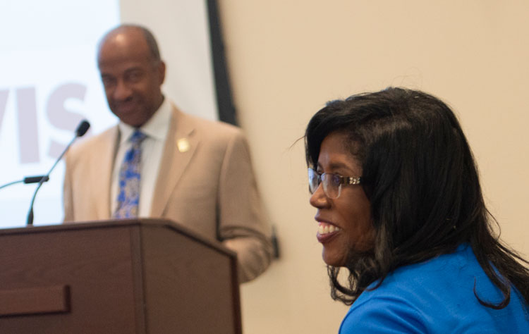 Sonja Colbert at meeting, with Chancellor May at podium, in the background