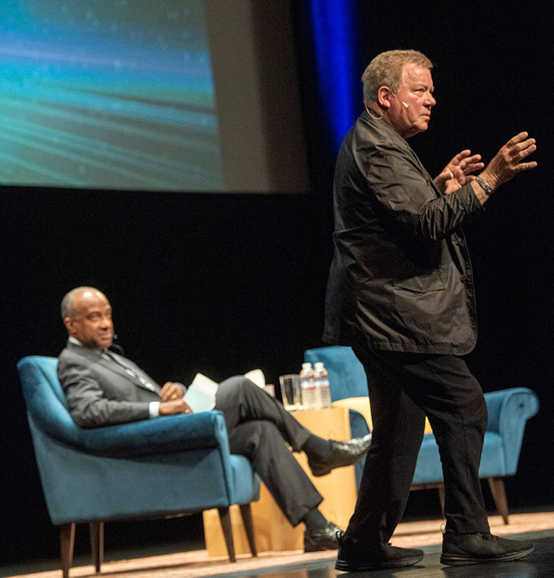 William Shatner on stage with Chancellor Gary S. May in the background.