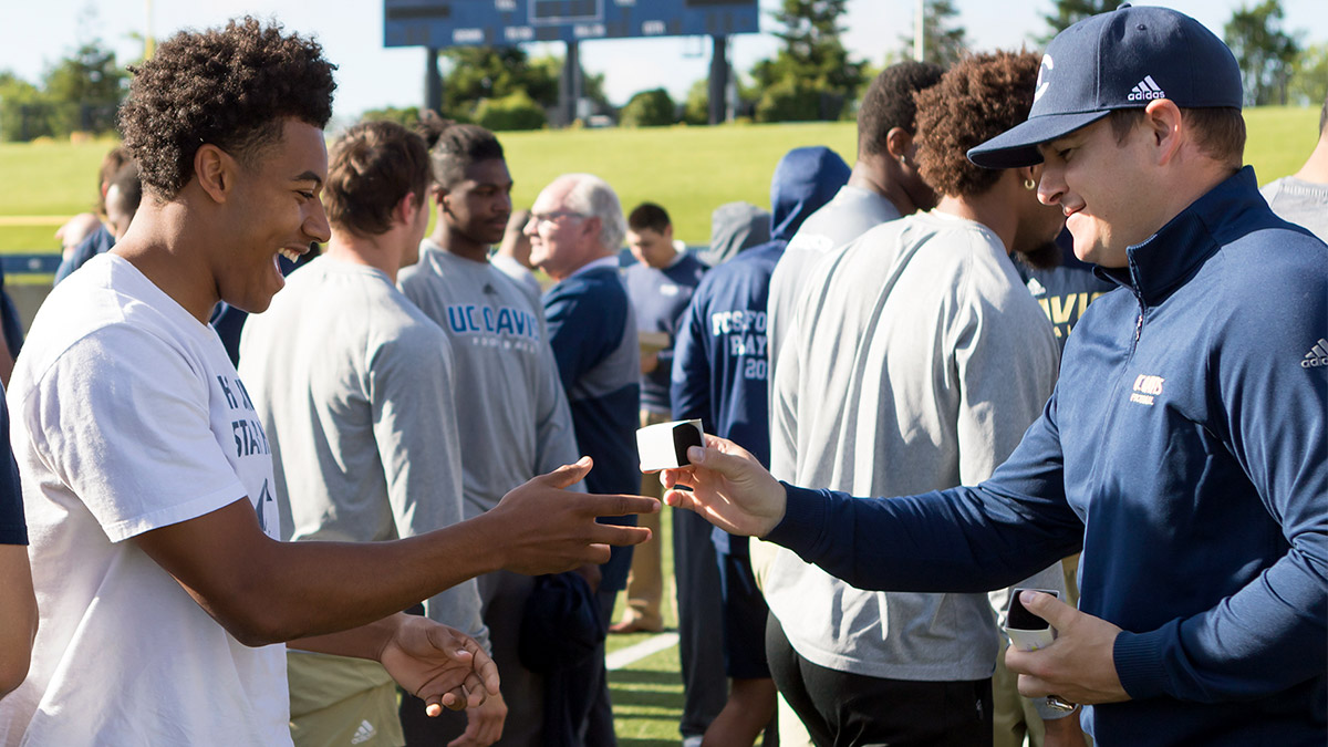 A coach hands a ring box to a football player.