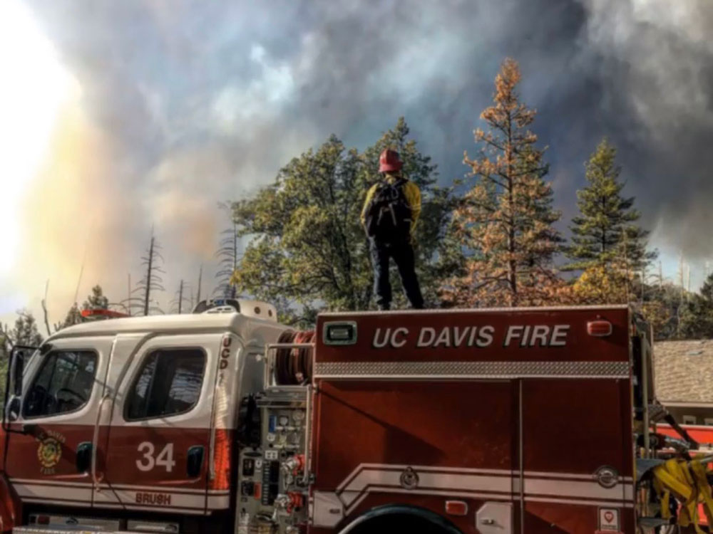 Firefighter stands atop Brush Truck 34, smoke billowing behind.