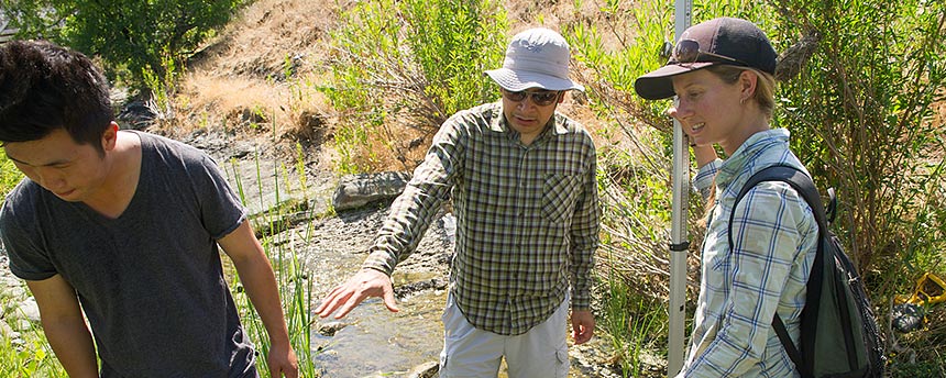 In the middle of a stream, a man in center pointing to woman on right while a man on the left looks the other way