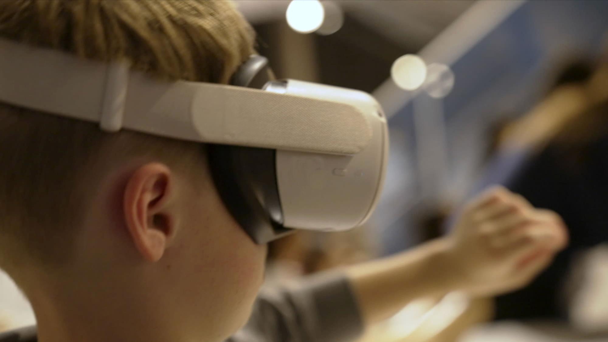 A student wearing a virtual reality headset and stretching their arms out in front of their face