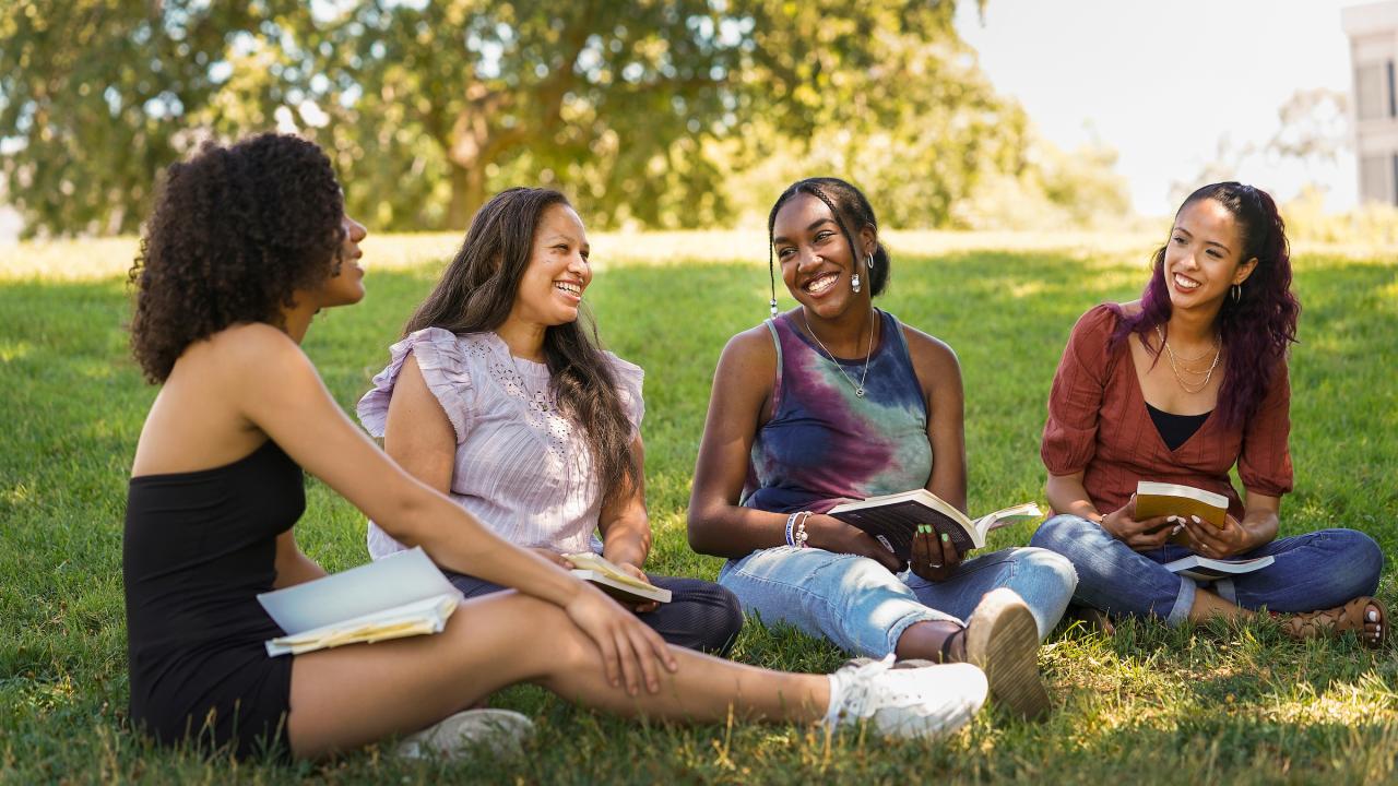 Three students and a staff member smile on the grass at UC Davis. 