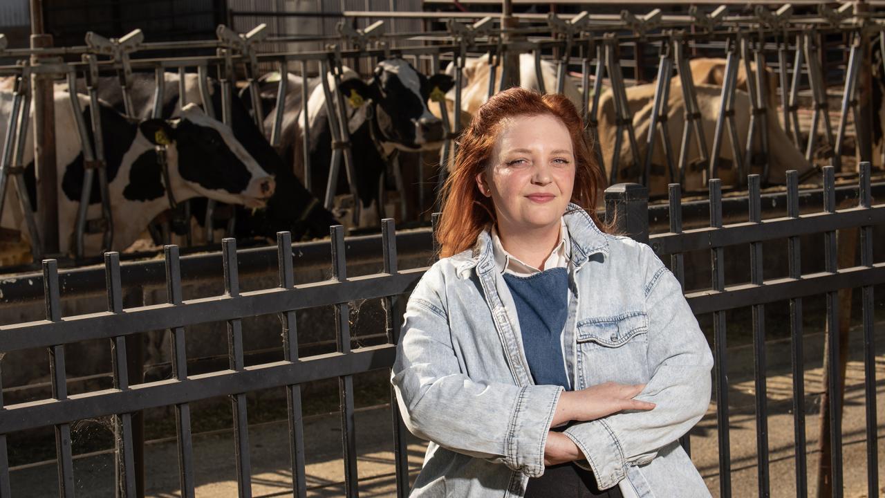 Caroline Williams stands in front of dairy cows at a trough.