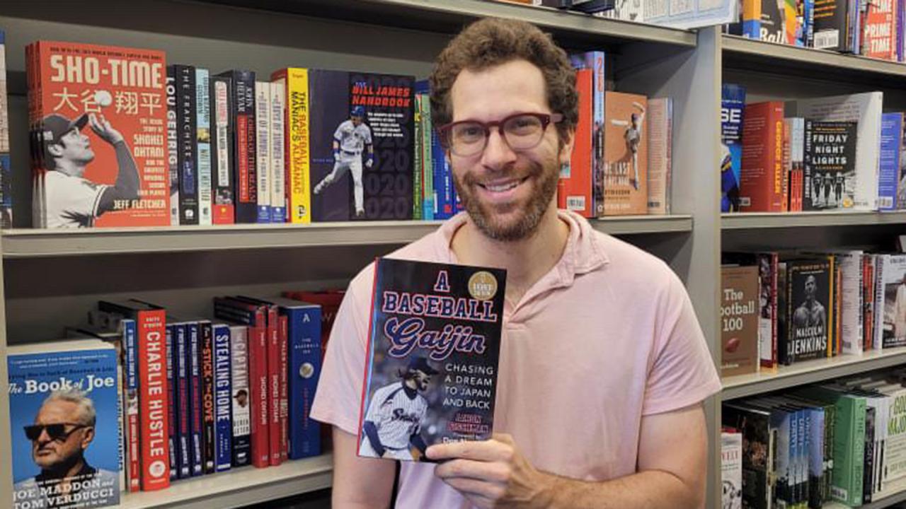 Man holds book in front of full bookshelf