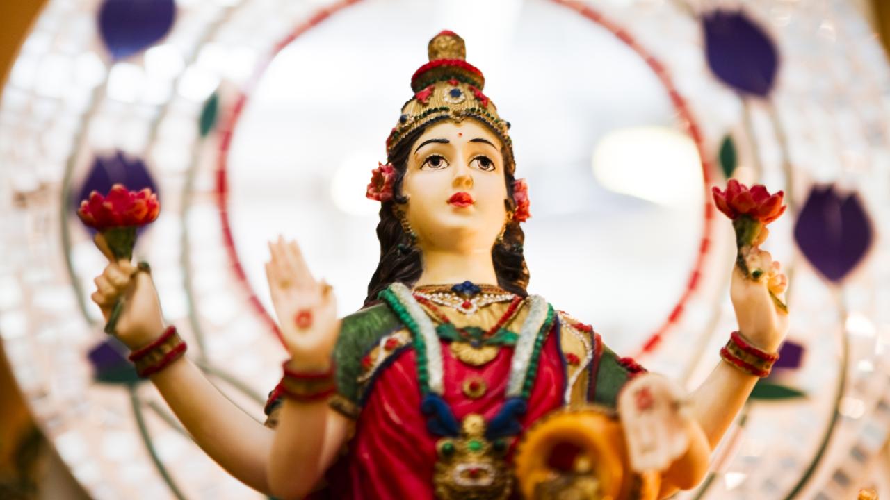 Hindu goddess statue of woman with dark hair holding red lotus bouquets in outstretched hands.