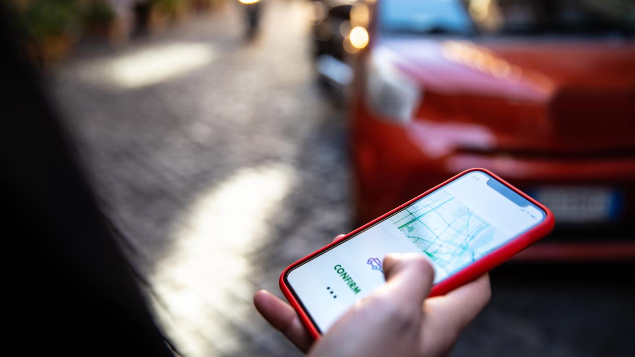 perrson holding phone with screen showing map as red car approaches 