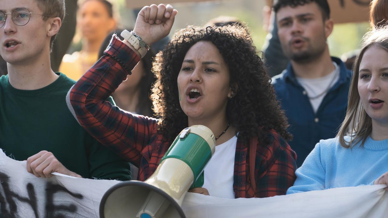 People in crowd holding signs, shouting into megaphone