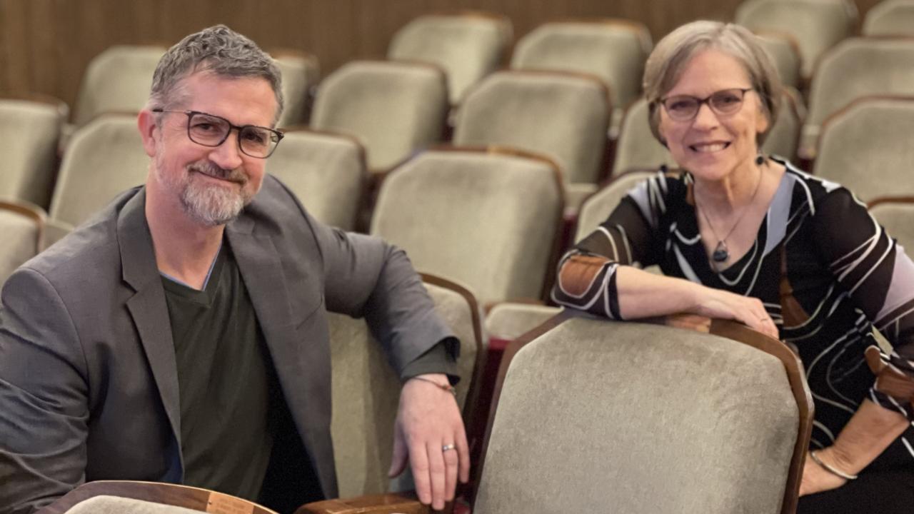 A man and a woman sitting in rows of folding seats