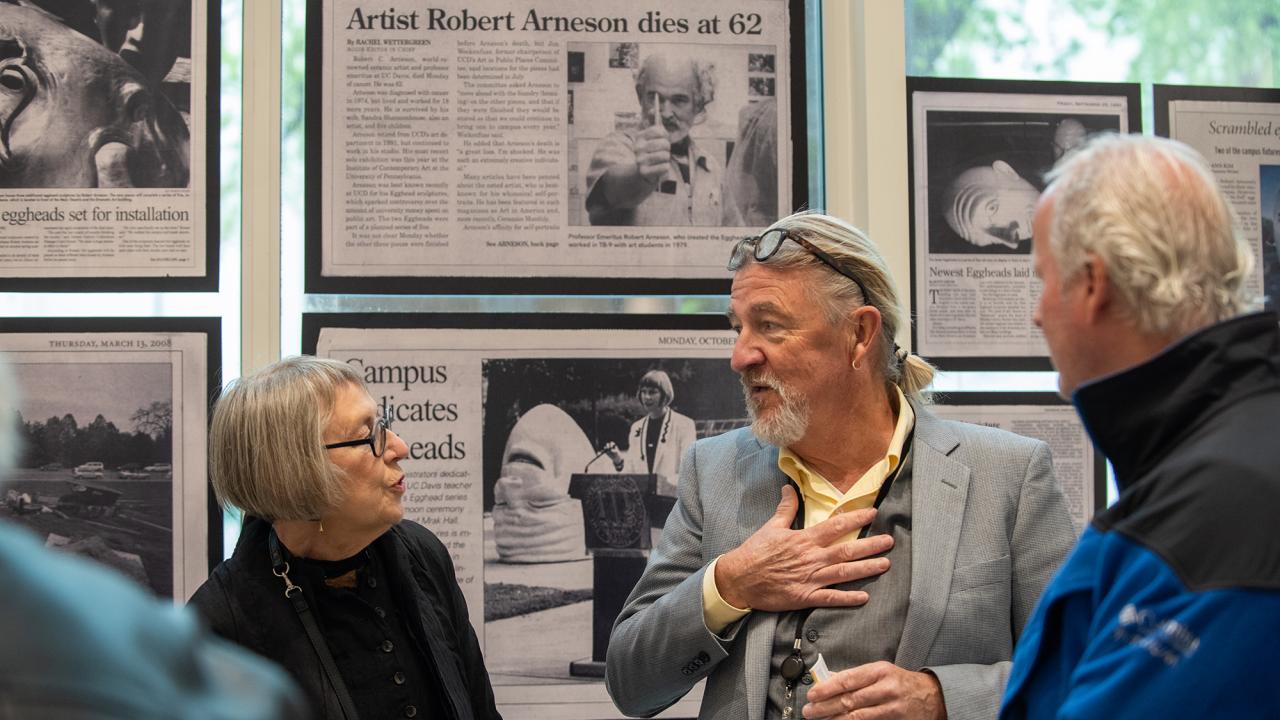 Three people stand in front of library exhibit on Robert Arneson