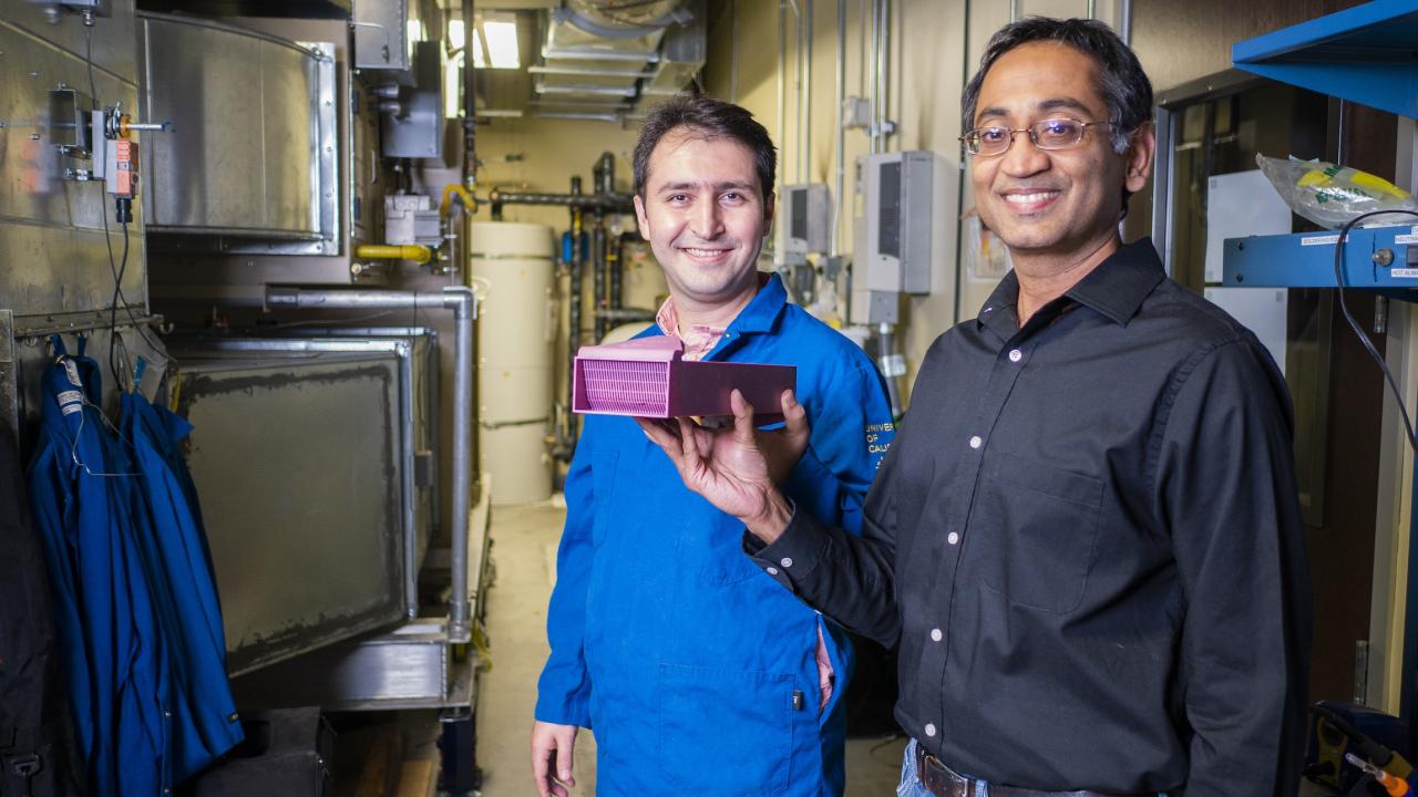 Scientists Erfan Rasouli in blue lab coat and Vinod Narayanan stand and smile in lab