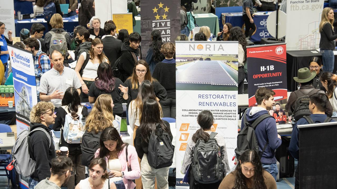 Many students crowd around employers and their banners at a career fair