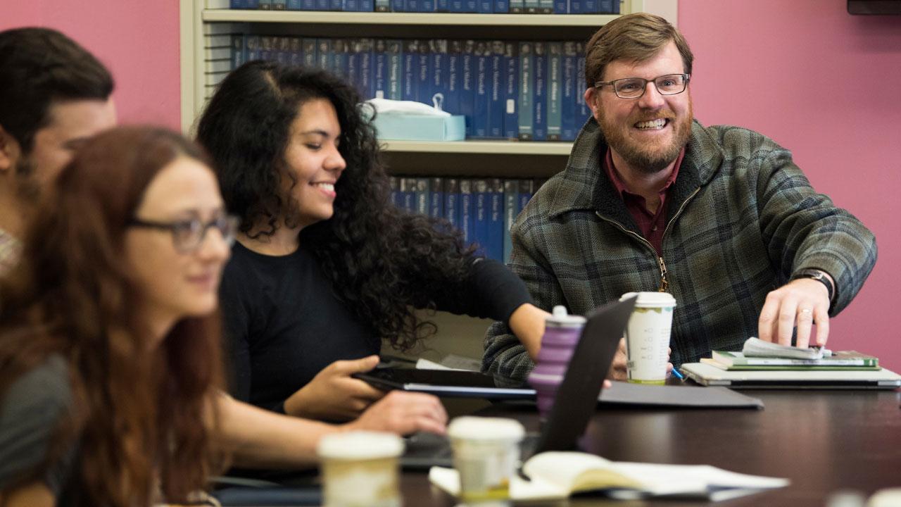 A mentor works with students at a large table