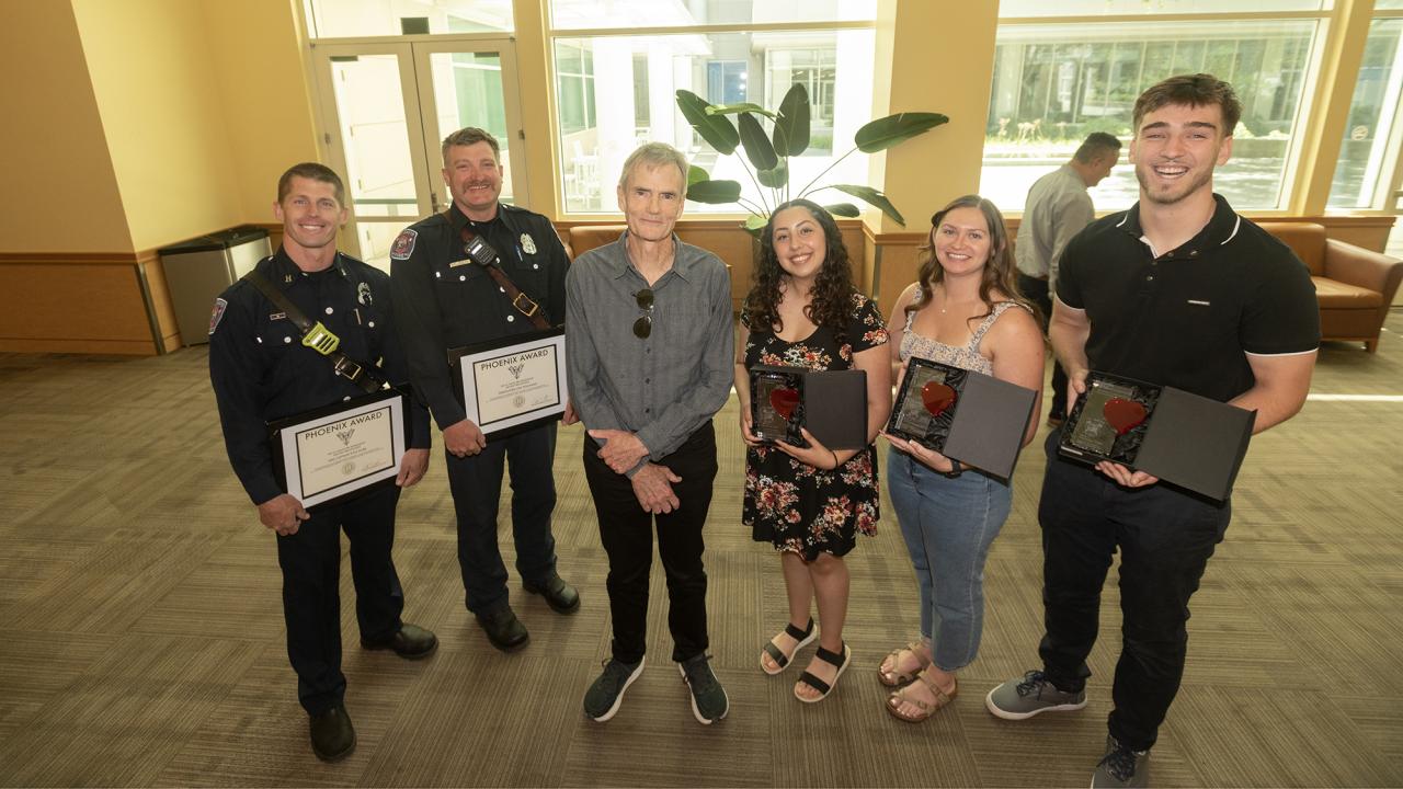 Two fire department personnel and three students flank the man they saved