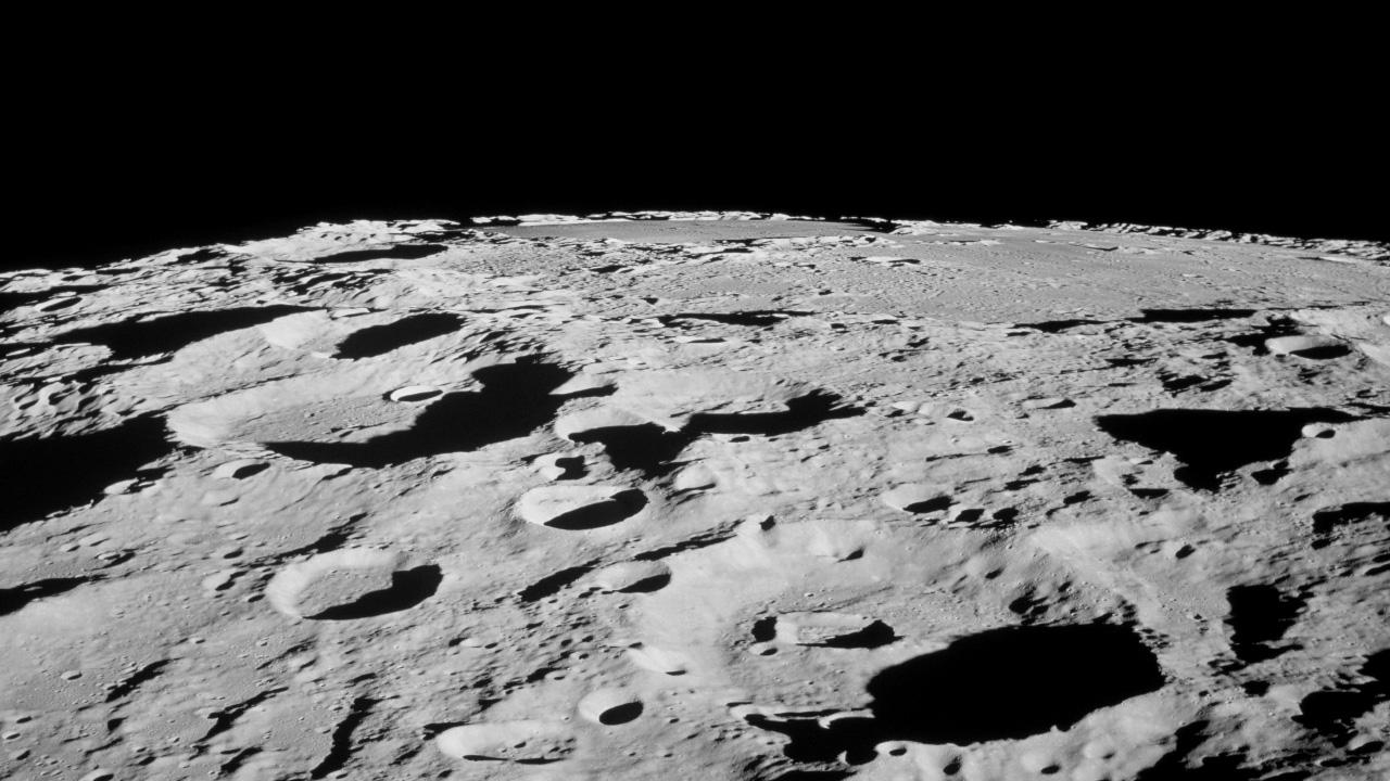 Monochrome view of a rocky, cratered plain with a black sky in the background.