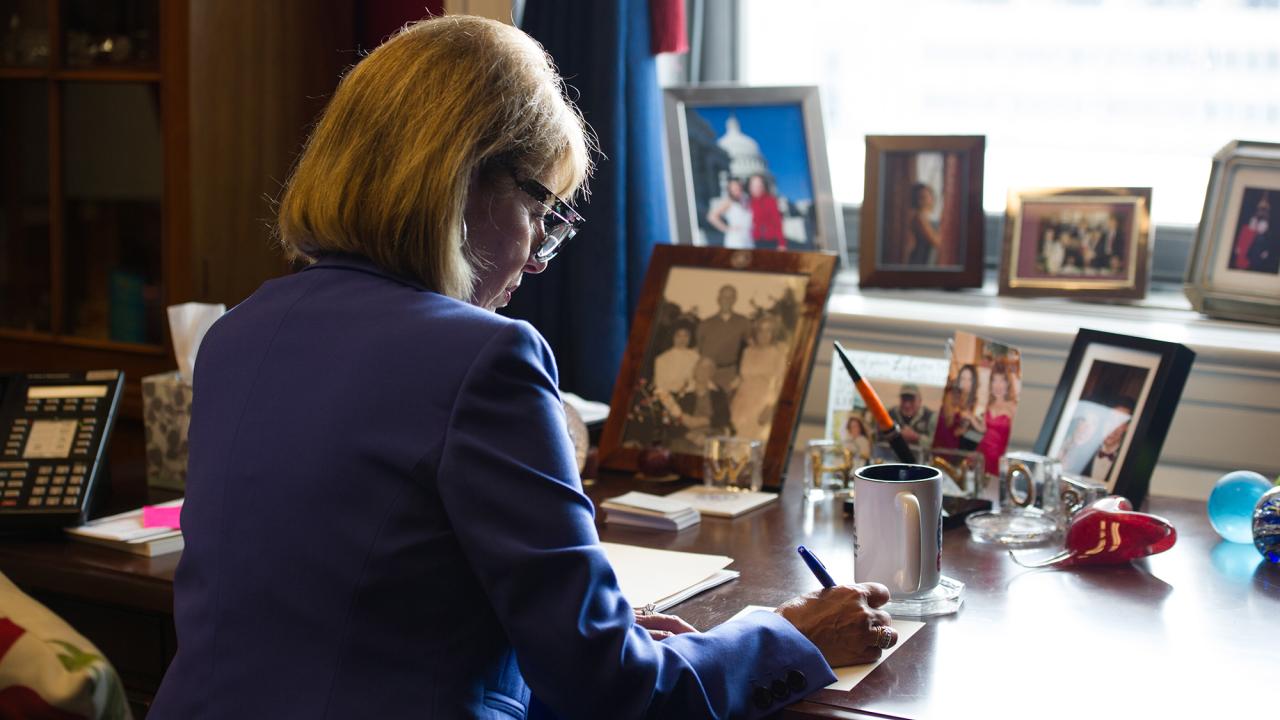 Woman sits at desk writing on paper