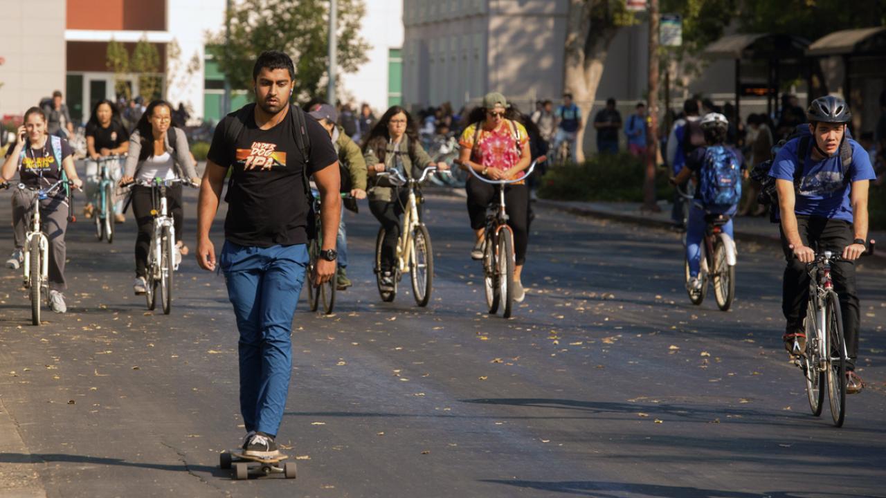 a student on a skateboard followed by others riding across campus - transfer students with special situations