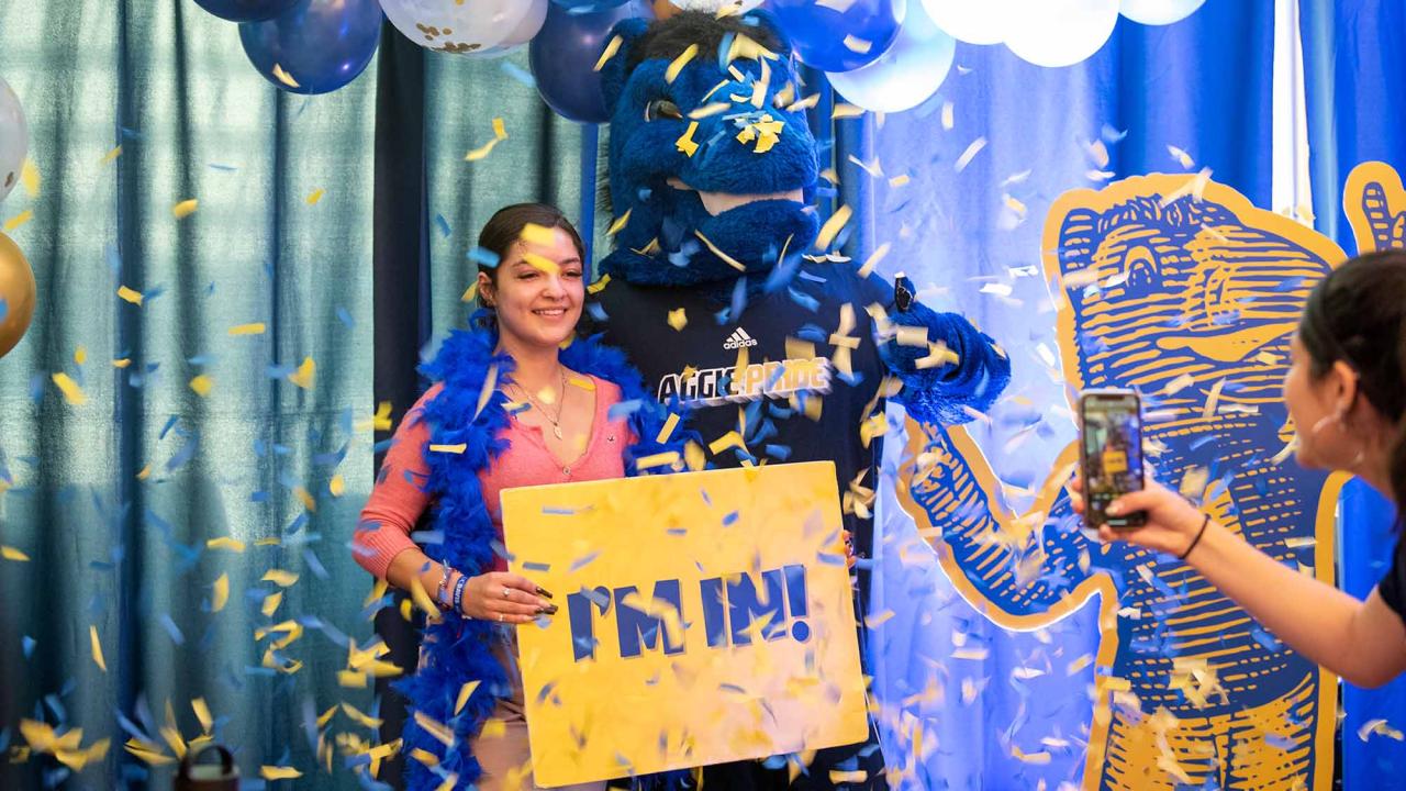 Student poses with Gunrock while holding gold sign reading "I'm in" as confetti falls