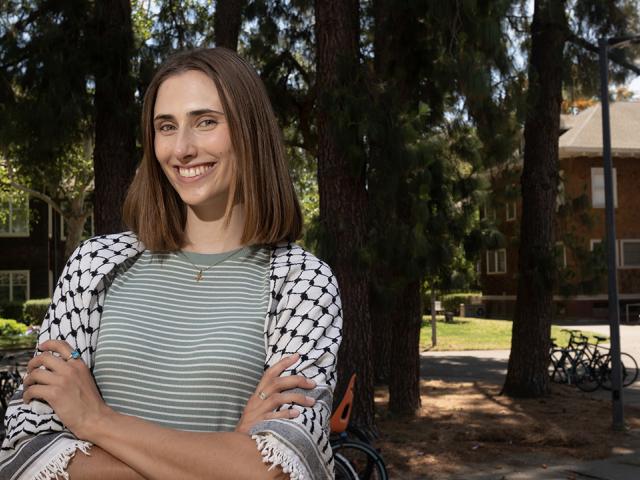 Brooke Morey wears a keffiyeh against a background of trees.